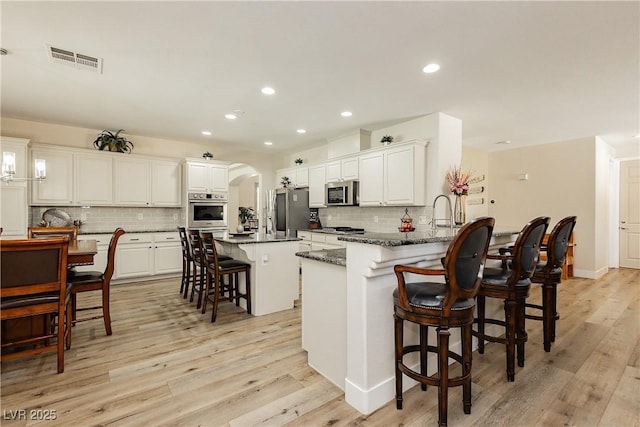 kitchen featuring a breakfast bar area, visible vents, light wood finished floors, arched walkways, and appliances with stainless steel finishes