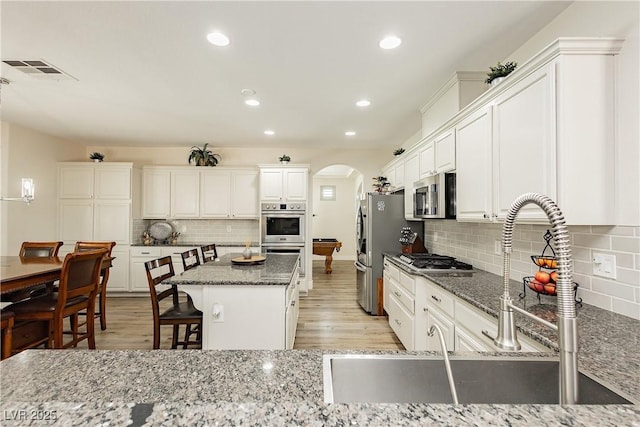 kitchen with visible vents, a kitchen bar, a kitchen island, stainless steel appliances, and arched walkways