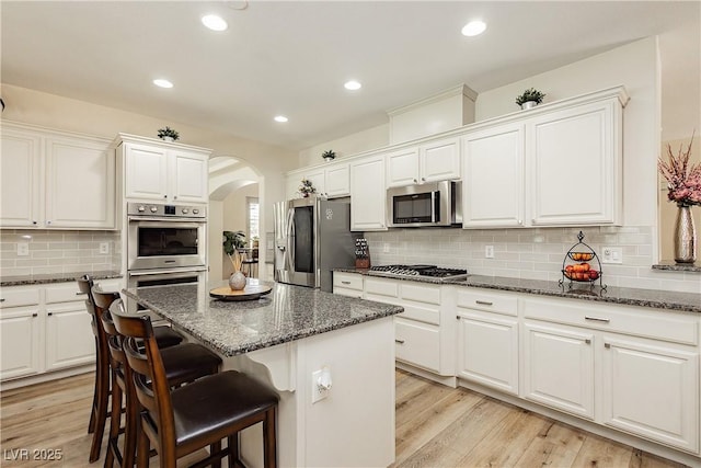 kitchen featuring arched walkways, light wood-style flooring, appliances with stainless steel finishes, and a kitchen island