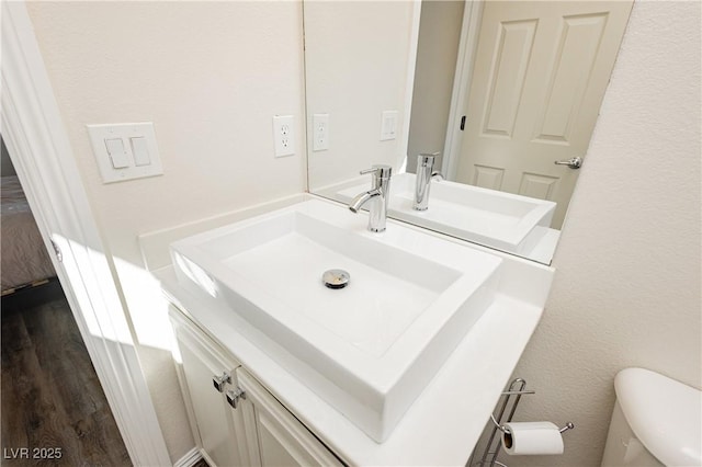 bathroom with toilet, vanity, and wood finished floors