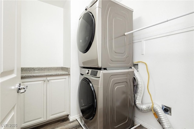 laundry area featuring cabinet space, stacked washer and clothes dryer, and wood finished floors