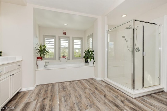 bathroom with a stall shower, wood finished floors, recessed lighting, baseboards, and a bath