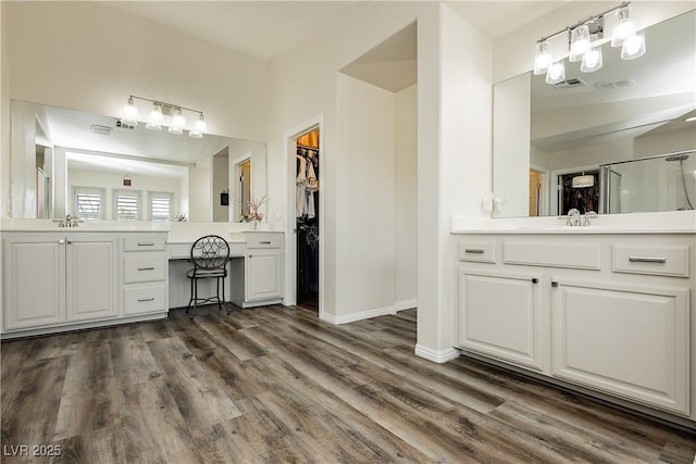 full bath with wood finished floors, baseboards, two vanities, a sink, and a spacious closet