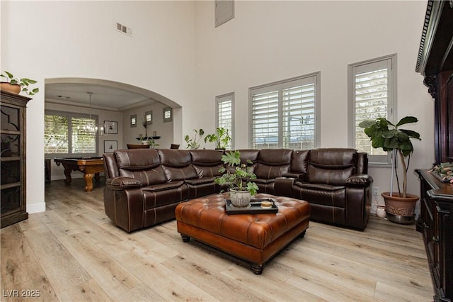 living room with visible vents, billiards, arched walkways, light wood finished floors, and a towering ceiling