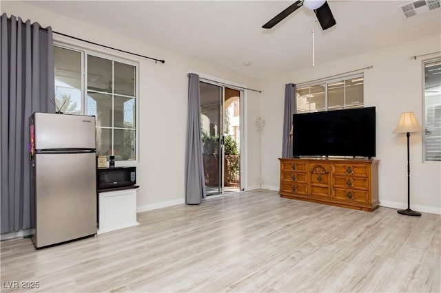 living room with ceiling fan, visible vents, baseboards, and light wood-style flooring