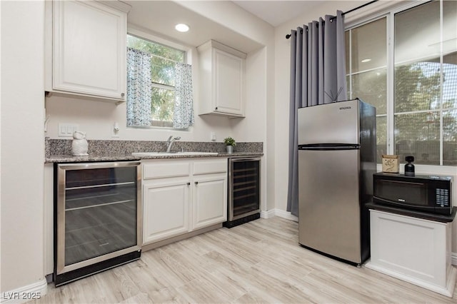 kitchen with a sink, beverage cooler, black microwave, and freestanding refrigerator