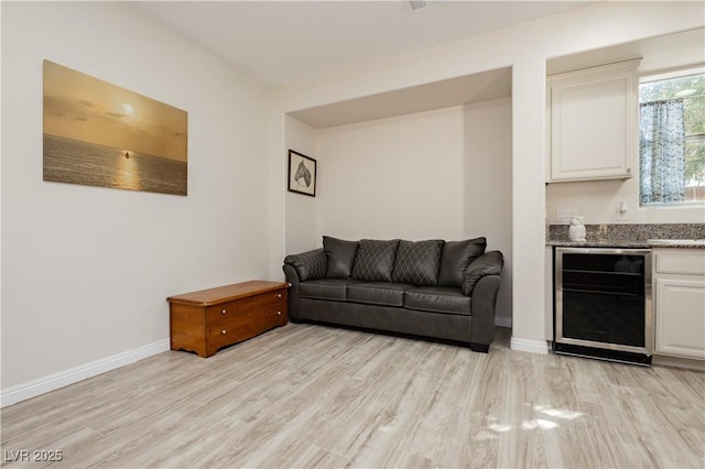 living room featuring beverage cooler, light wood finished floors, a dry bar, and baseboards