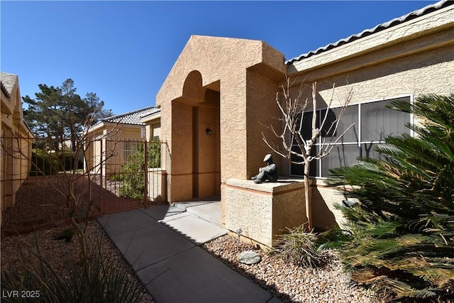 exterior space with stucco siding, a tile roof, and a gate