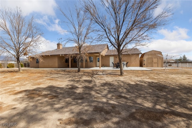 view of front of house featuring fence, a shed, stucco siding, an outdoor structure, and a patio