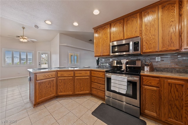 kitchen with light tile patterned floors, brown cabinets, appliances with stainless steel finishes, and a peninsula