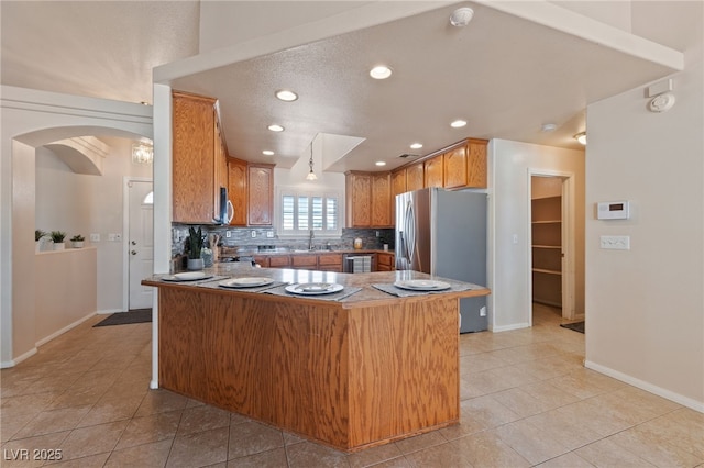 kitchen featuring a sink, tasteful backsplash, arched walkways, a peninsula, and stainless steel fridge with ice dispenser