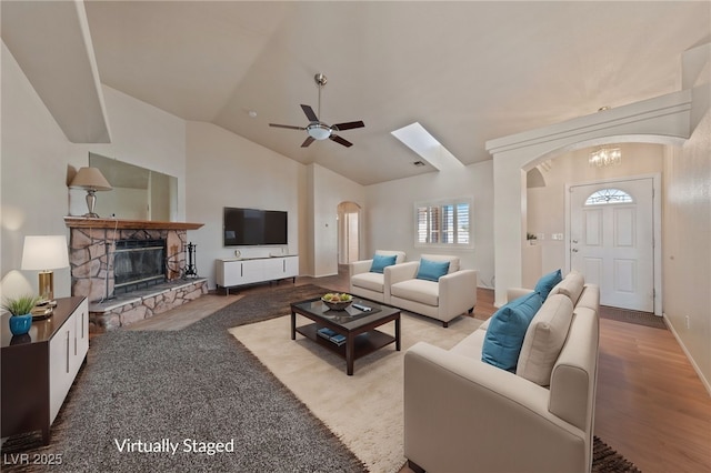 living area featuring vaulted ceiling, ceiling fan with notable chandelier, a fireplace, wood finished floors, and arched walkways