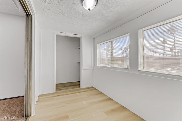 corridor with a textured ceiling and light wood finished floors