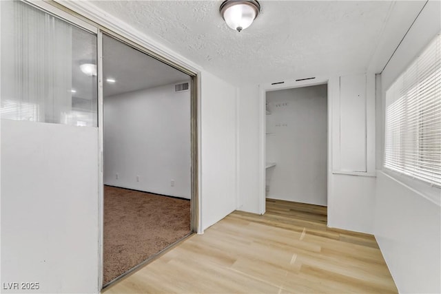 corridor with visible vents, light wood-style floors, and a textured ceiling