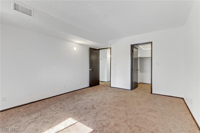 unfurnished bedroom with visible vents, a walk in closet, a textured ceiling, carpet flooring, and baseboards