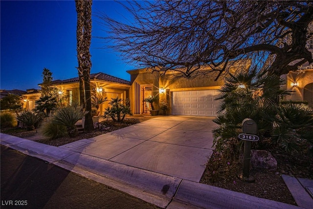 view of front facade with a tile roof, concrete driveway, a garage, and stucco siding