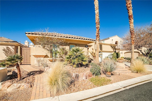 mediterranean / spanish-style home featuring stucco siding, a garage, driveway, and a gate