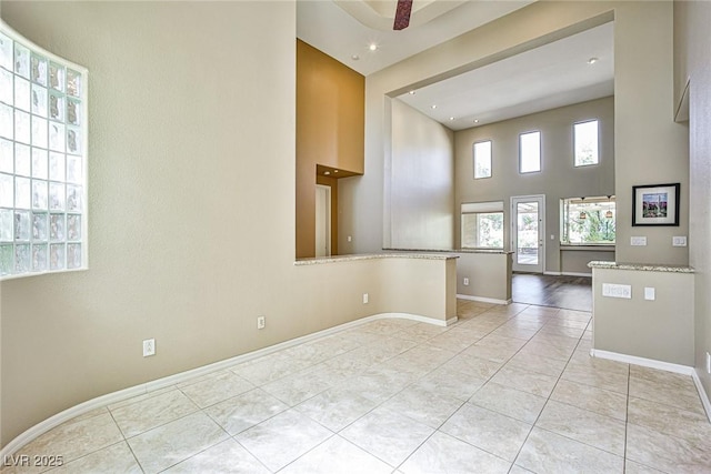 spare room with light tile patterned flooring, baseboards, and a towering ceiling