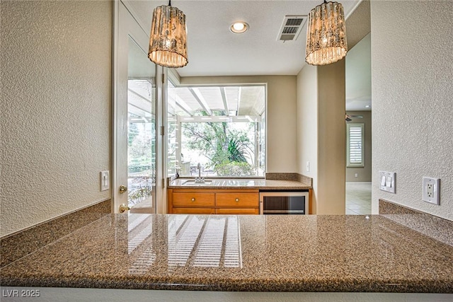 kitchen featuring visible vents, a sink, wine cooler, pendant lighting, and a textured wall