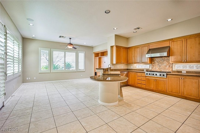 kitchen with a sink, backsplash, stainless steel appliances, a peninsula, and wall chimney exhaust hood