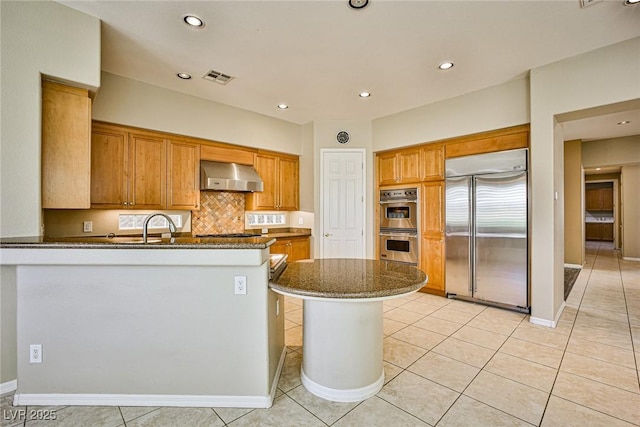 kitchen with a peninsula, wall chimney exhaust hood, light tile patterned floors, and stainless steel appliances