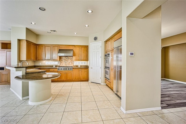 kitchen featuring ventilation hood, appliances with stainless steel finishes, a peninsula, and light tile patterned floors