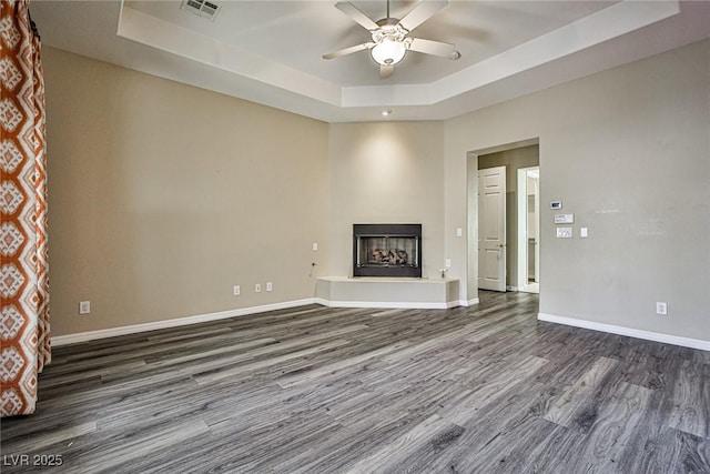 unfurnished living room featuring visible vents, a raised ceiling, baseboards, and a fireplace with raised hearth