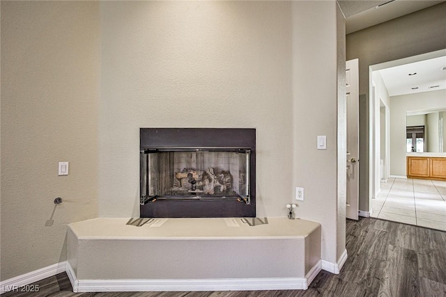 room details featuring baseboards, a fireplace with raised hearth, and wood finished floors