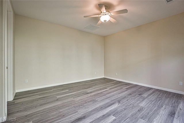 empty room with a ceiling fan, visible vents, wood finished floors, and baseboards