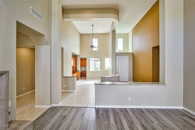 interior space with a ceiling fan, visible vents, baseboards, a high ceiling, and light wood-style floors