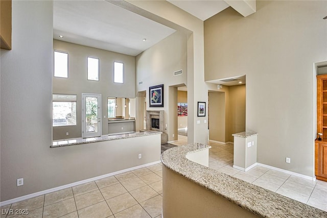 interior space featuring light tile patterned floors, a glass covered fireplace, baseboards, and visible vents