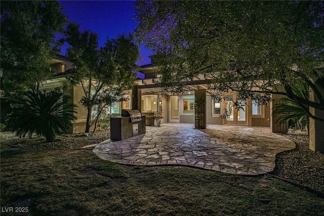 back of house at twilight featuring stucco siding, a patio area, french doors, and an outdoor kitchen