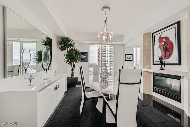 dining space featuring a fireplace, an inviting chandelier, a healthy amount of sunlight, and a tray ceiling