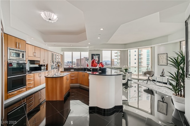 kitchen with light tile patterned floors, a kitchen island, a tray ceiling, recessed lighting, and stainless steel microwave