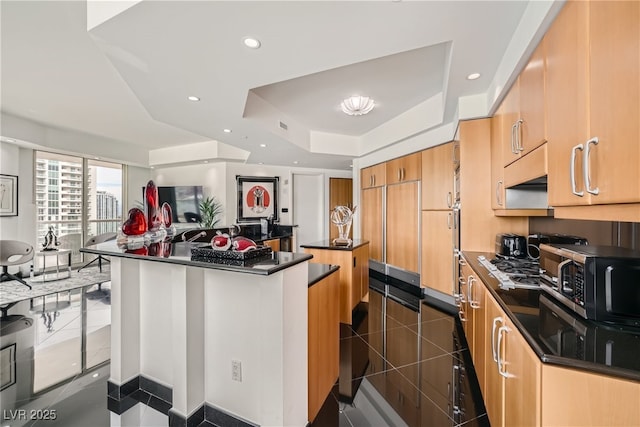 kitchen with dark countertops, a tray ceiling, recessed lighting, a large island with sink, and dark tile patterned flooring