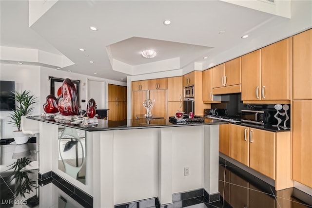 kitchen featuring a tray ceiling, recessed lighting, built in appliances, under cabinet range hood, and dark countertops