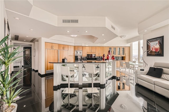 kitchen with stainless steel microwave, dark countertops, visible vents, and light brown cabinetry