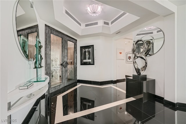 hall featuring tile patterned floors, baseboards, a raised ceiling, and visible vents