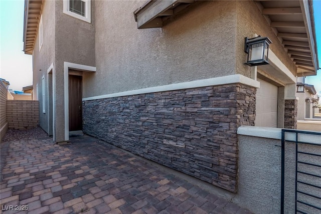 view of side of property featuring stucco siding, stone siding, a garage, and fence