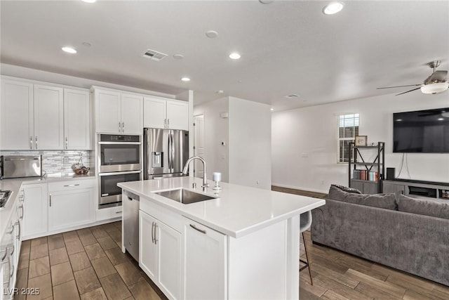 kitchen featuring wood finish floors, a sink, backsplash, open floor plan, and appliances with stainless steel finishes