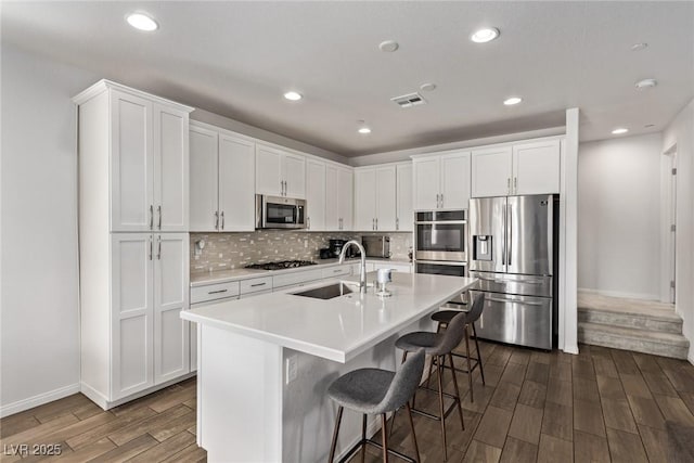 kitchen with dark wood-style floors, visible vents, a sink, appliances with stainless steel finishes, and tasteful backsplash