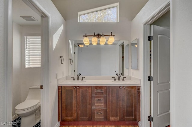 bathroom with a sink, visible vents, toilet, and double vanity