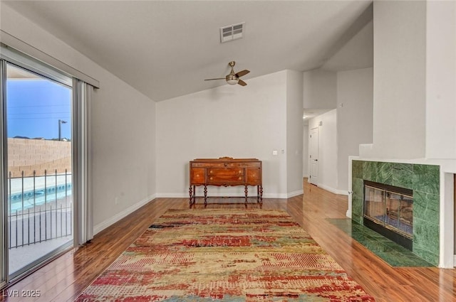 interior space with visible vents, wood finished floors, baseboards, vaulted ceiling, and a tile fireplace