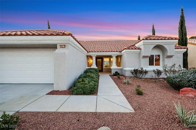 mediterranean / spanish-style house with stucco siding, an attached garage, a tile roof, and concrete driveway