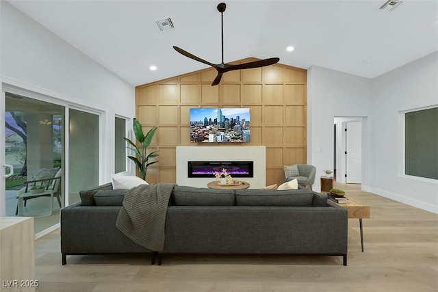 living room with a glass covered fireplace, light wood-style floors, visible vents, and ceiling fan