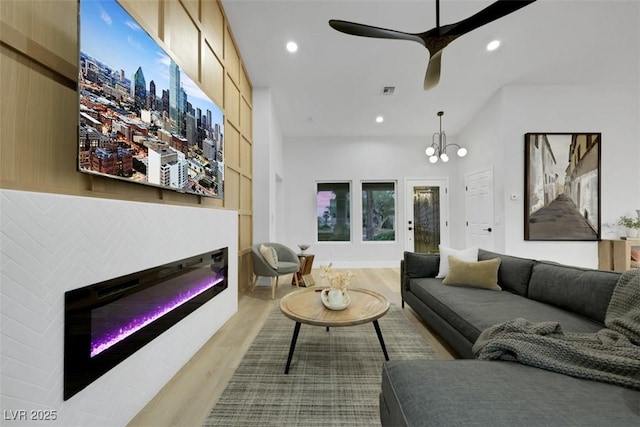 living area featuring a glass covered fireplace, recessed lighting, ceiling fan with notable chandelier, and wood finished floors