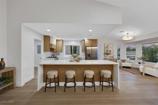 kitchen featuring a breakfast bar, light countertops, stainless steel refrigerator with ice dispenser, and light wood finished floors