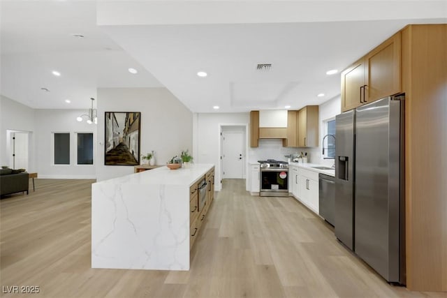 kitchen featuring light wood-type flooring, visible vents, a sink, light stone counters, and stainless steel appliances