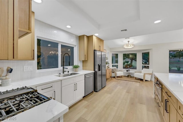 kitchen featuring light stone countertops, visible vents, a sink, light wood-style floors, and appliances with stainless steel finishes