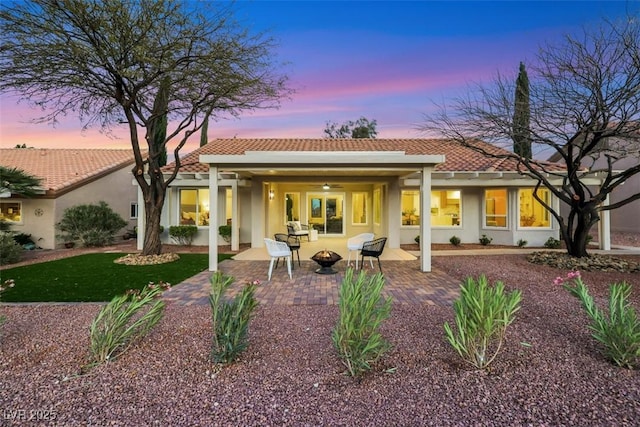 back of property at dusk featuring a fire pit, a tile roof, a patio area, and stucco siding